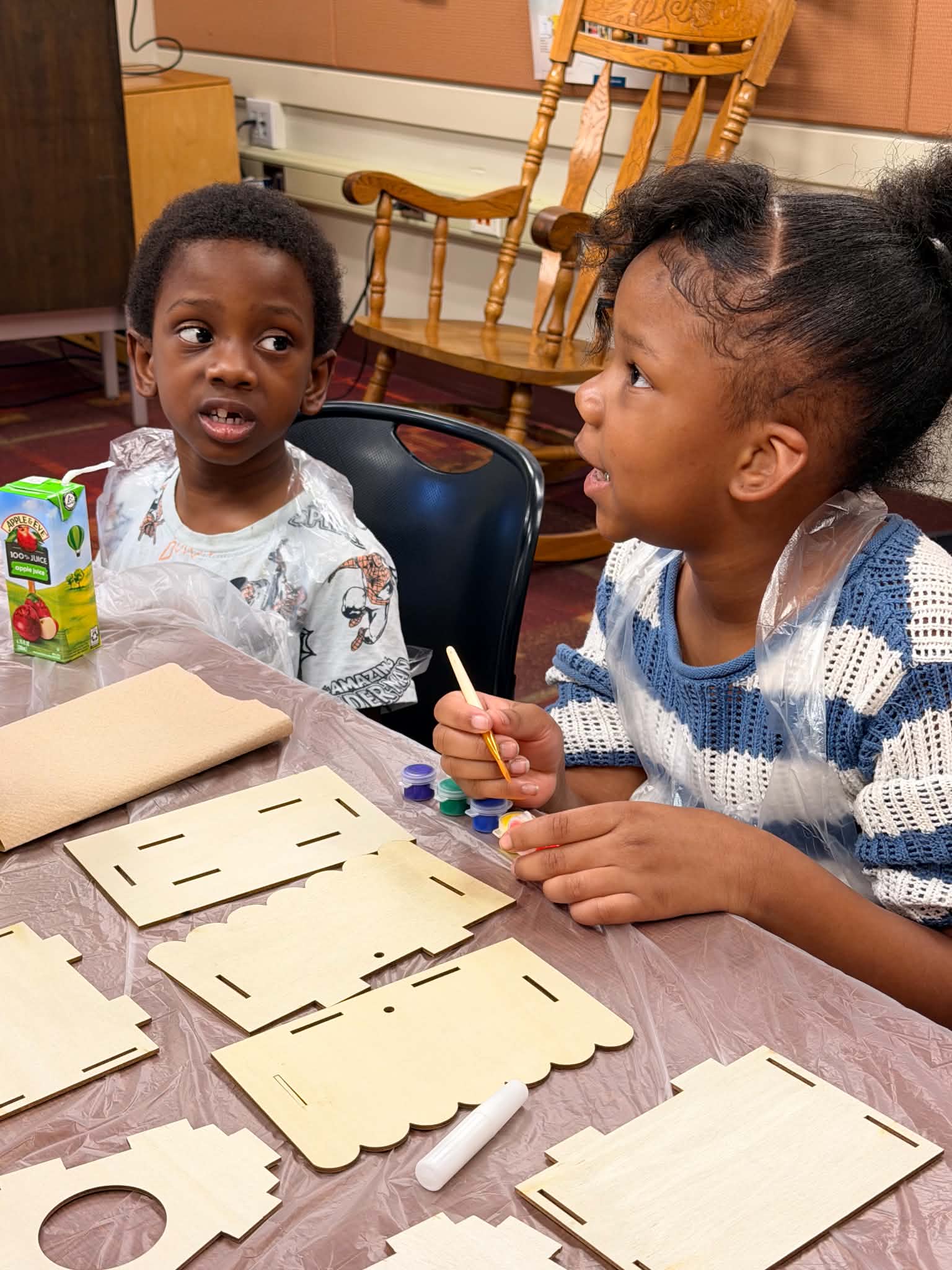 Children seated beside unfinished wooden art pieces during a hands-on workshop activity.