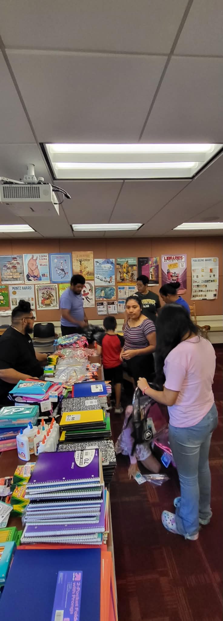 Families gather around tables filled with notebooks, glue, and school supplies during a Back to School event.