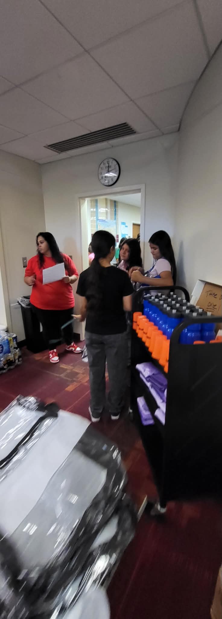 Students stand near a cart of water bottles and event supplies during a Back to School giveaway.
