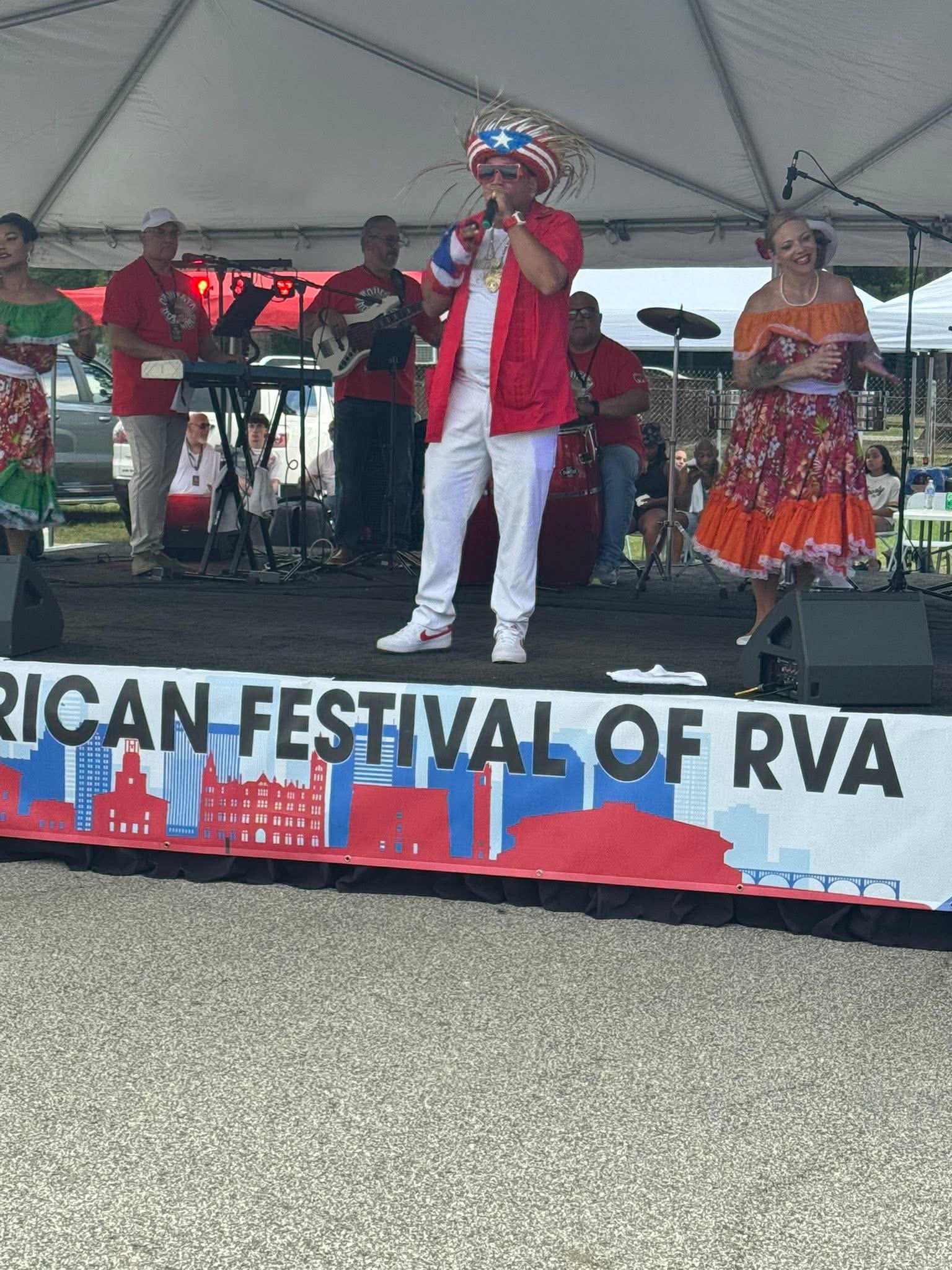 Two people pose beside a Puerto Rican flag and a community booth at the Puerto Rican Festival.