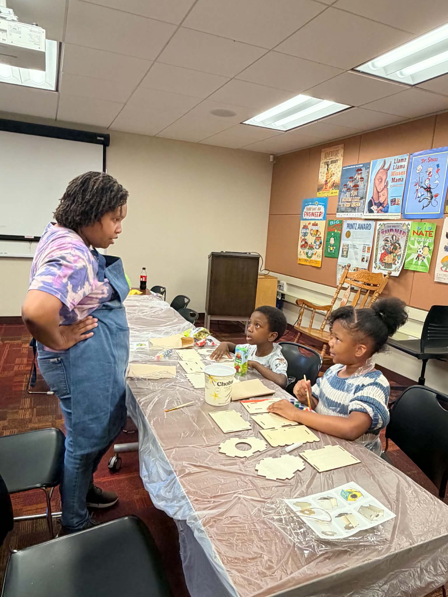 An adult facilitator guiding children at a table during a Rising Up Now art workshop.