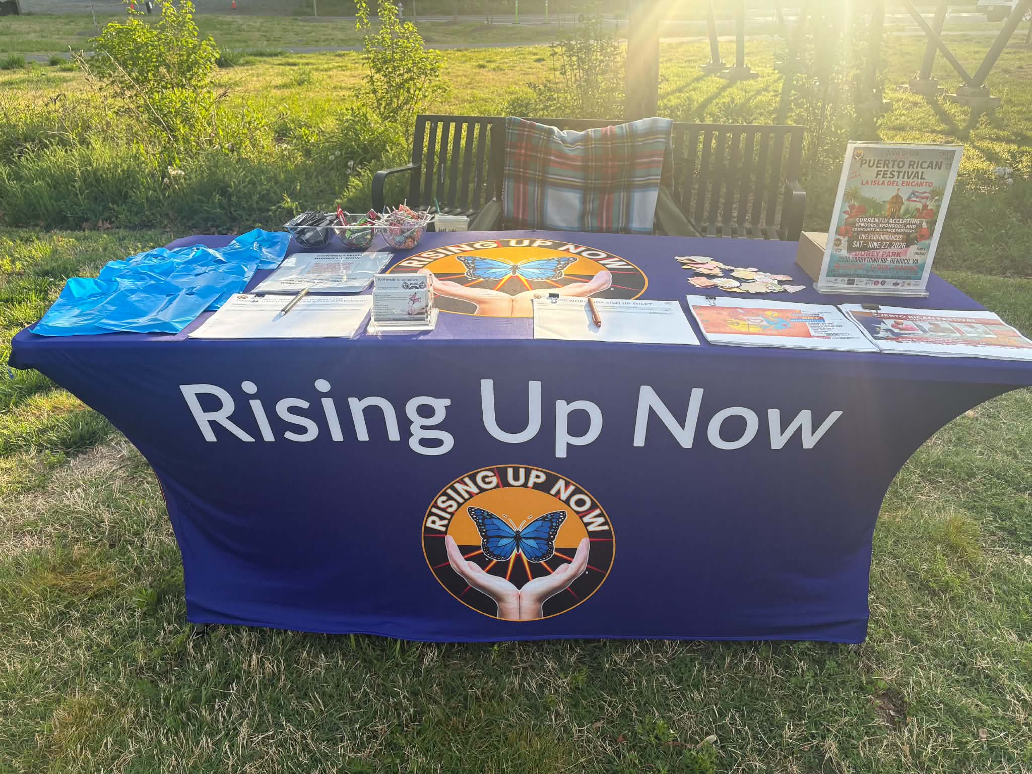 A Rising Up Now table display set up at the Puerto Rican Festival with flyers, sign-up sheets, and candy.