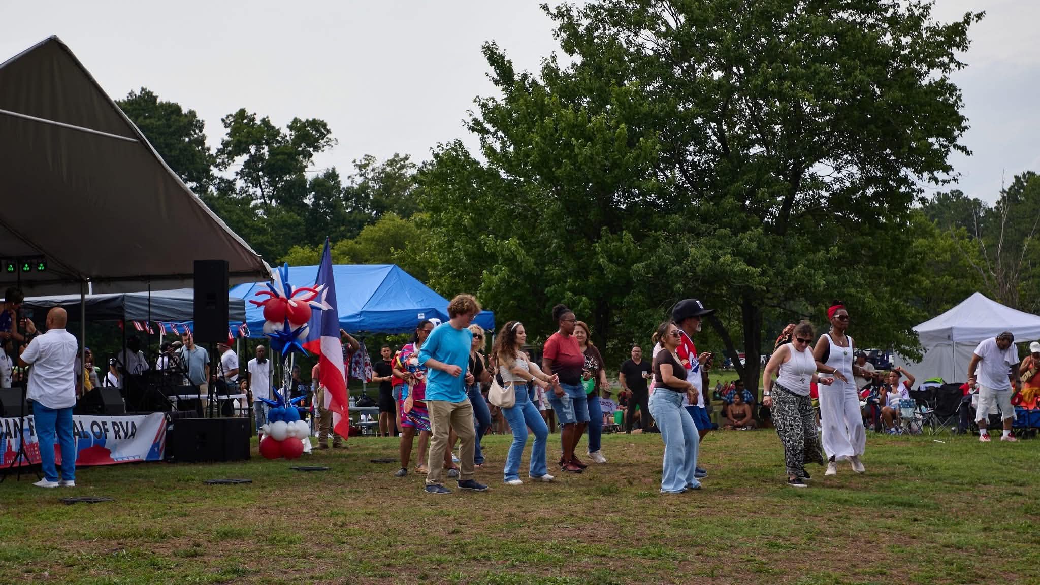 Festival attendees dance in front of the stage beside Puerto Rican flags and balloons.