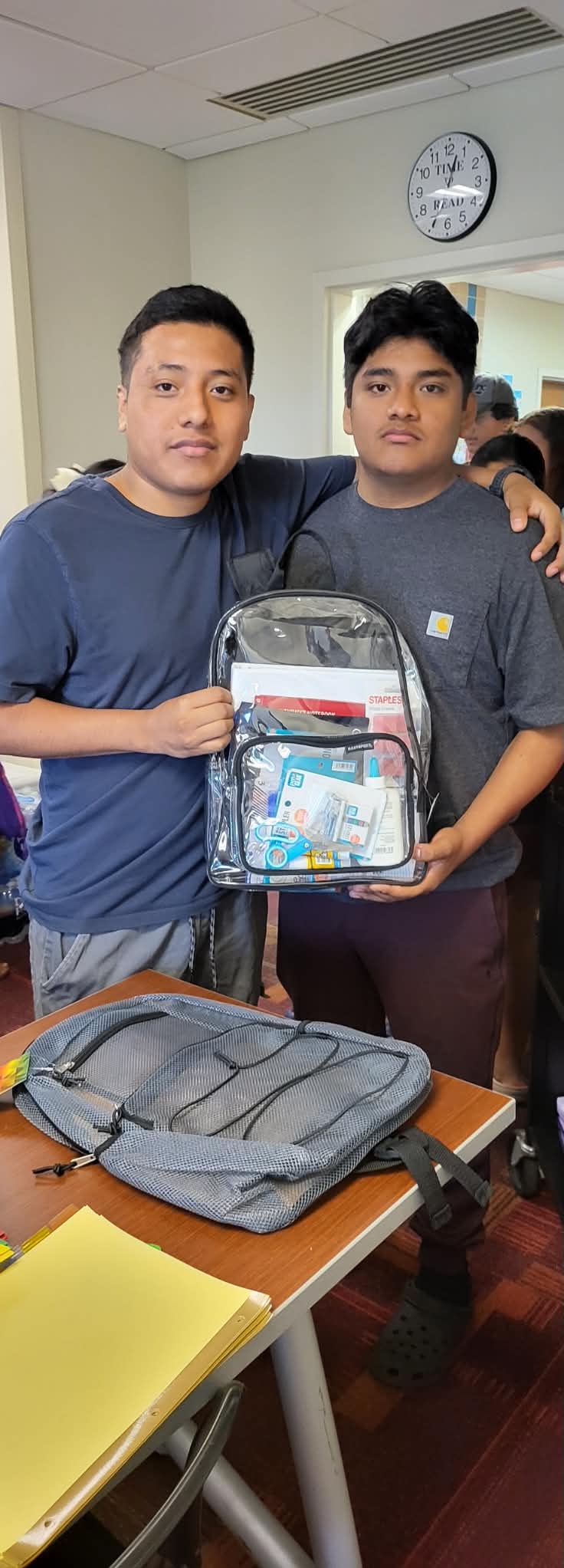 Two students pose with a clear backpack filled with school supplies at a Back to School event.