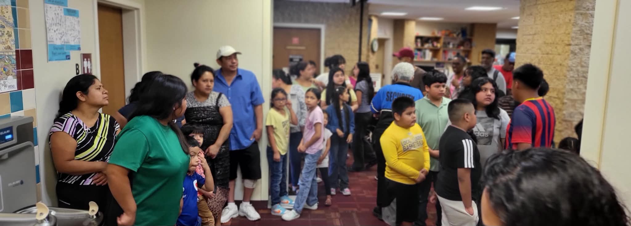Families and children gather in a hallway before receiving supplies at a Back to School event.